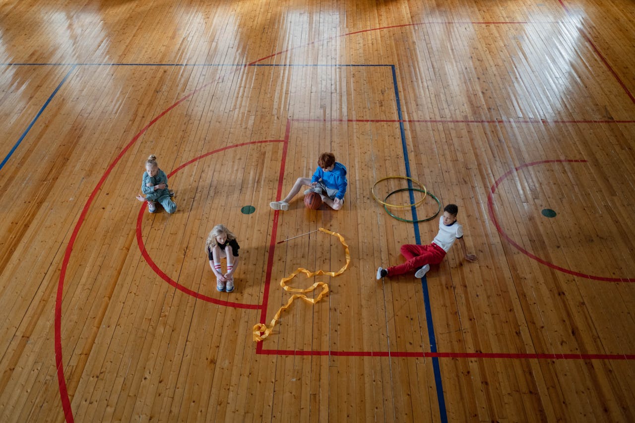 Children relaxing on a gym floor with sports equipment around them.